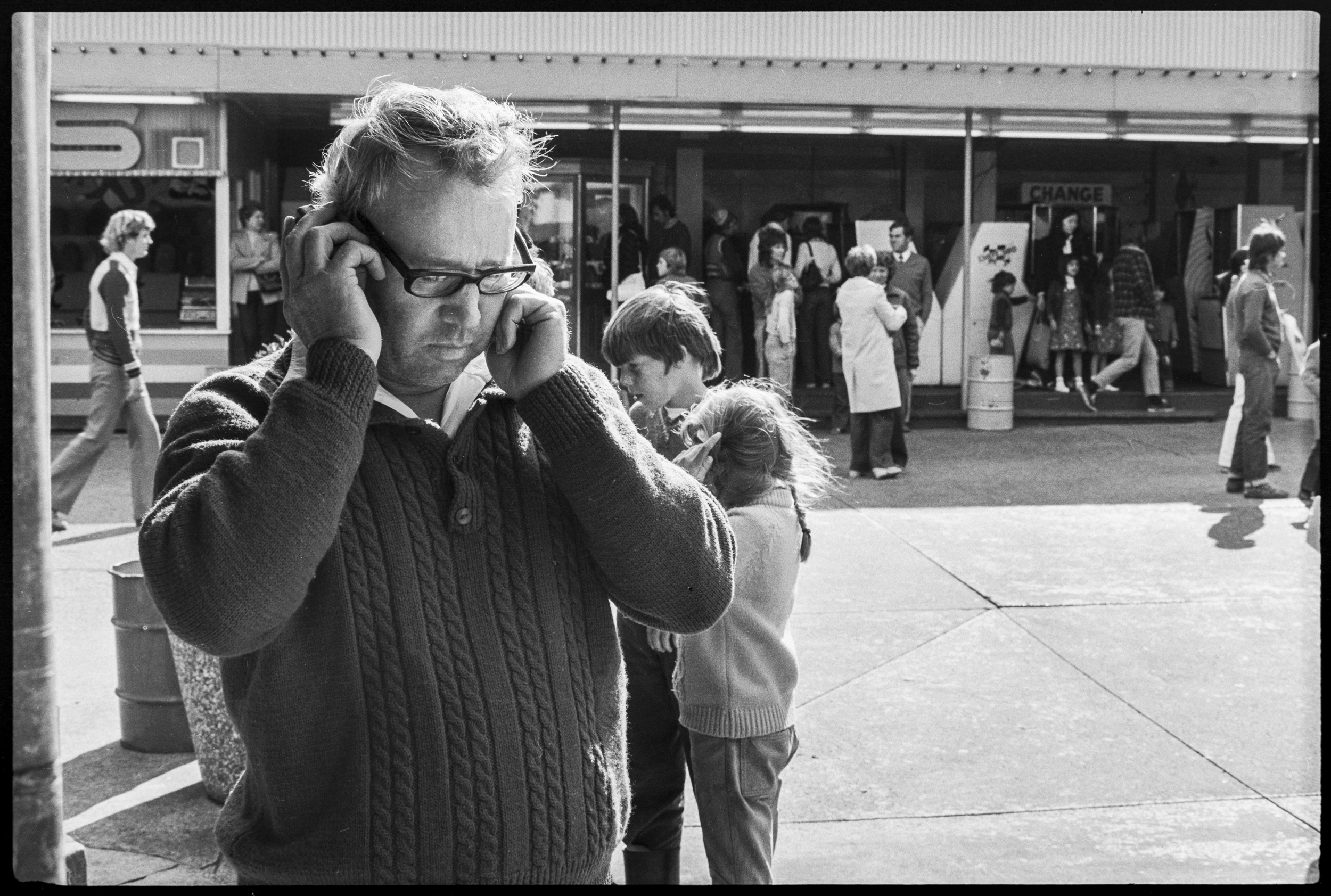 46 75 36 and 46 75 37 St Kilda Luna Park. General scenes of visitors. In 2 of the images a man listens to the races on his transistor radio held to his ear. He could also be listening to the latest football scores. It was VERY common for people to walk